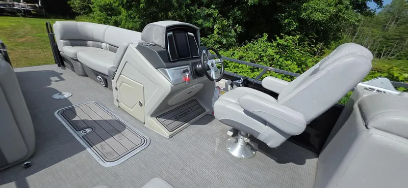 Slide: The Image of 2022 Regency 230 LE3 boat interior with helm, seating, and lush greenery background. - 10