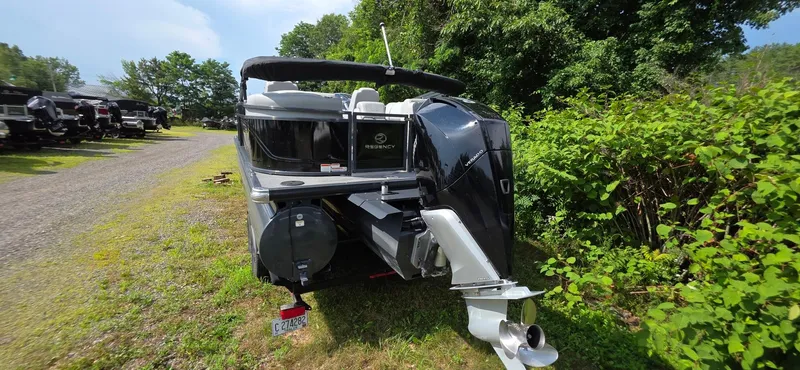 Slide: The Image of 2022 Regency 230 LE3 boat parked on grass near trees and other boats. - 18