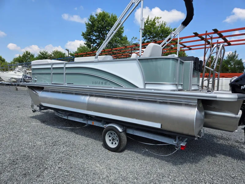 Slide: The Image of 2026 Harris Cruiser 210 pontoon boat on trailer, parked outdoors under blue sky. - 2