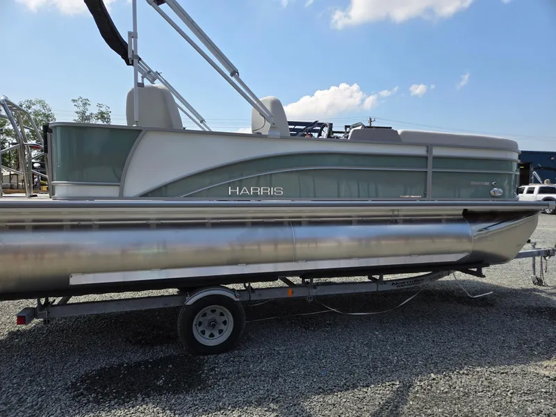 Slide: The Image of 2026 Harris Cruiser 210 pontoon boat on a trailer, parked on gravel. - 6