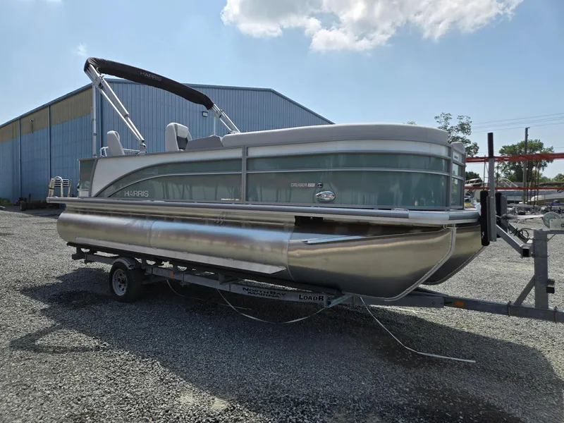 Slide: The Image of 2026 Harris Cruiser 210 pontoon boat on trailer, parked outdoors under a partly cloudy sky. - 7