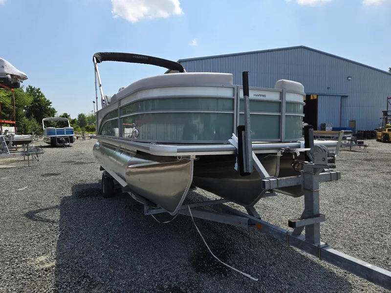 Slide: The Image of 2026 Harris Cruiser 210 pontoon boat on trailer, parked outdoors near a warehouse. - 8