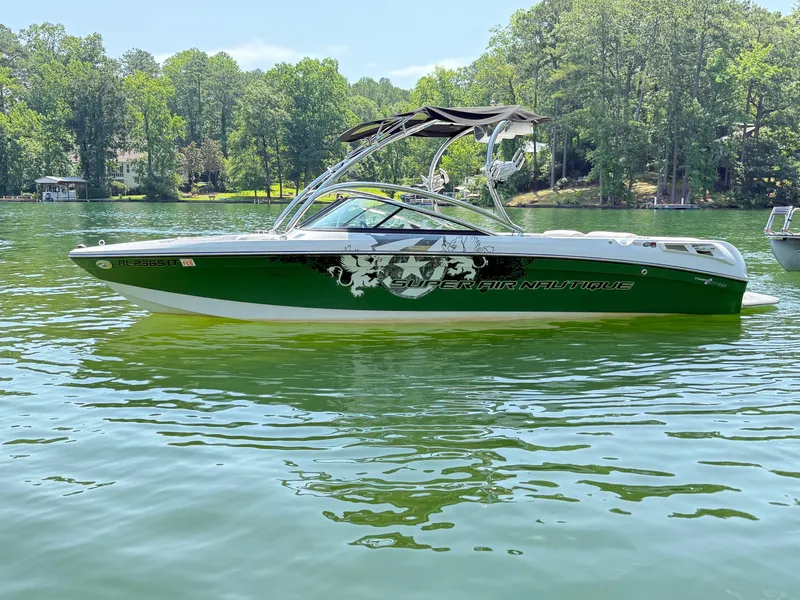 Slide: The Image of 2008 Nautique Super Air 230 boat on a serene lake with lush green surroundings. - 20