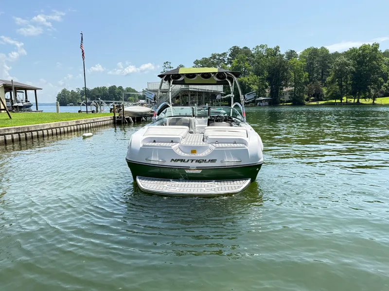 Slide: The Image of 2008 Nautique Super Air 230 boat docked on a sunny lake with trees in the background. - 3