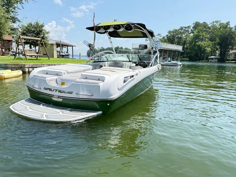 Slide: The Image of 2008 Nautique Super Air 230 boat on a serene lake with lush surroundings. - 4