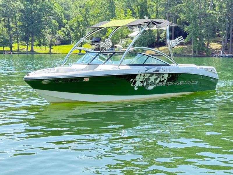 Slide: The Image of 2008 Nautique Super Air 230 boat on a serene lake with lush green surroundings. - 7
