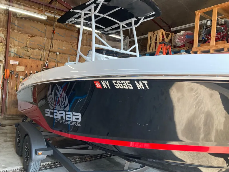 Slide: The Image of 2022 Wellcraft 202 Fisherman boat in garage, black hull with red stripe, Scarab Offshore logo. - 38