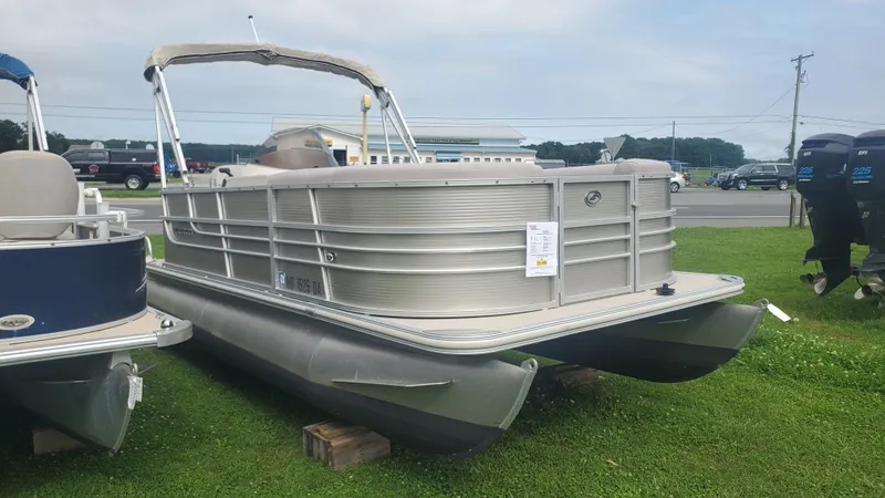 Slide: The Image of 2014 Starcraft SD 190 pontoon boat displayed on grass, with nearby vehicles and equipment. - 3