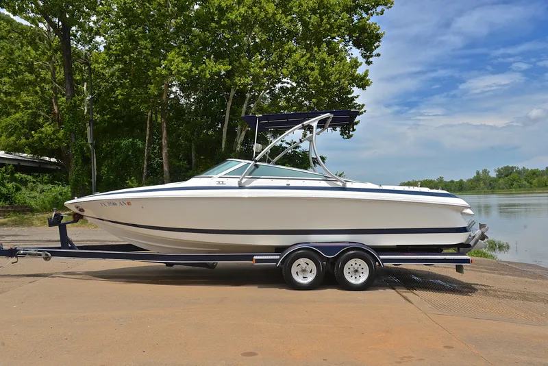 Slide: The Image of 2000 Cobalt 246 boat on trailer by a lake, surrounded by trees and clear sky. - 12