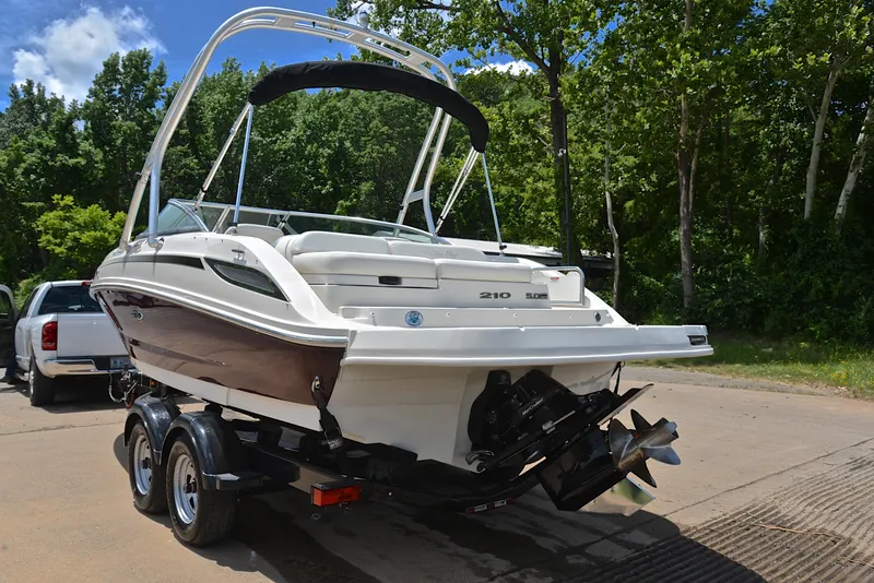 Slide: The Image of 2009 Sea Ray 210 Sundeck boat on trailer, parked outdoors with trees in background. - 12