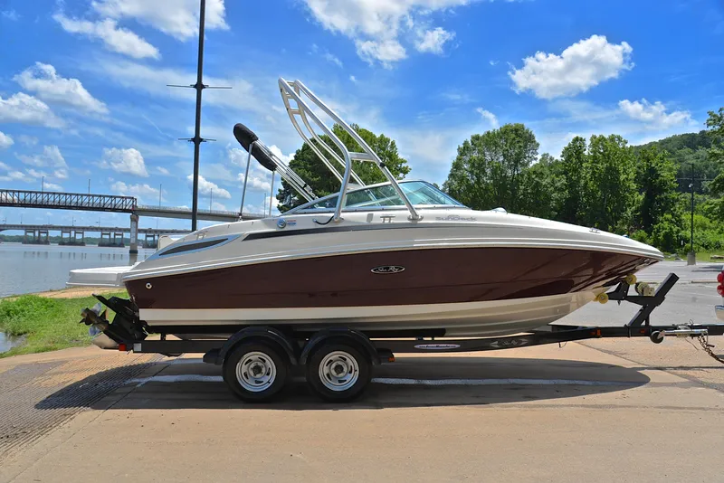 Slide: The Image of 2009 Sea Ray 210 Sundeck boat on trailer by a river, under a clear blue sky. - 15