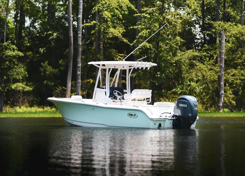 Slide: The Image of 2025 Sea Hunt Ultra 219 boat on calm water, surrounded by lush trees. - 17