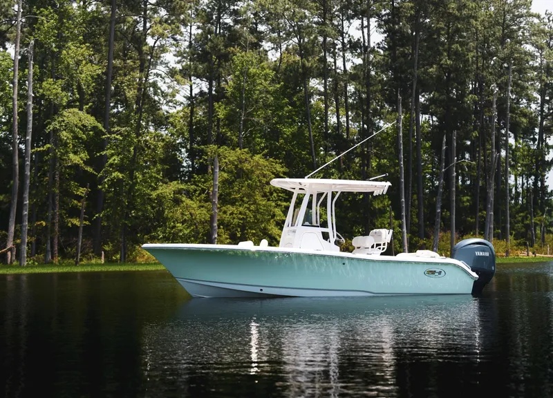 Slide: The Image of 2025 Sea Hunt Ultra 219 boat on a serene lake with forest backdrop. - 2
