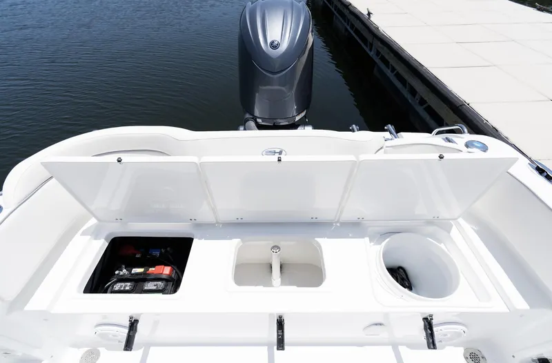 Slide: The Image of 2025 Sea Hunt Ultra 219 boat with open storage compartments and motor, docked by the water. - 8