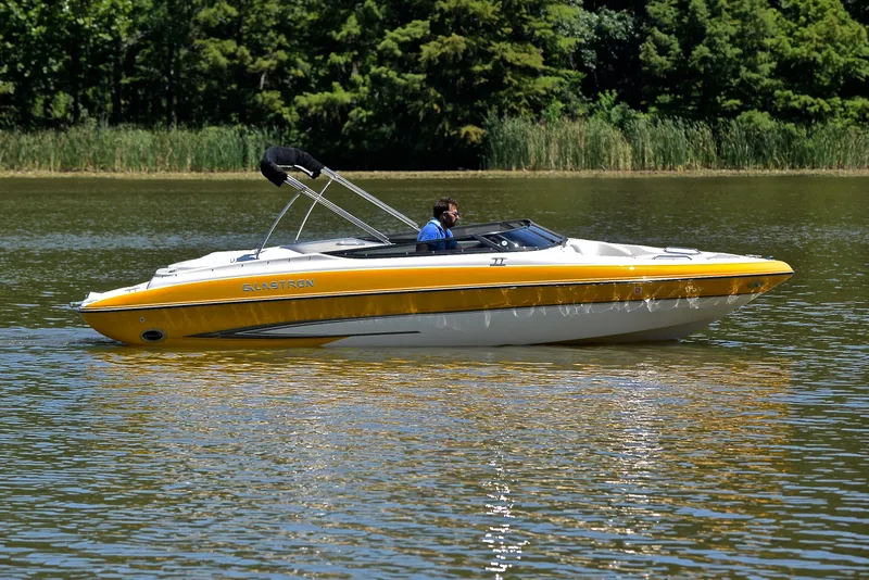 Slide: The Image of 2007 Glastron GXL 235 boat cruising on a calm lake with lush greenery. - 6