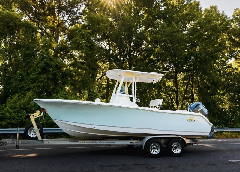 Slide: The Image of 2025 Sea Hunt Ultra 229 boat on trailer, parked on road with trees in background. - 20