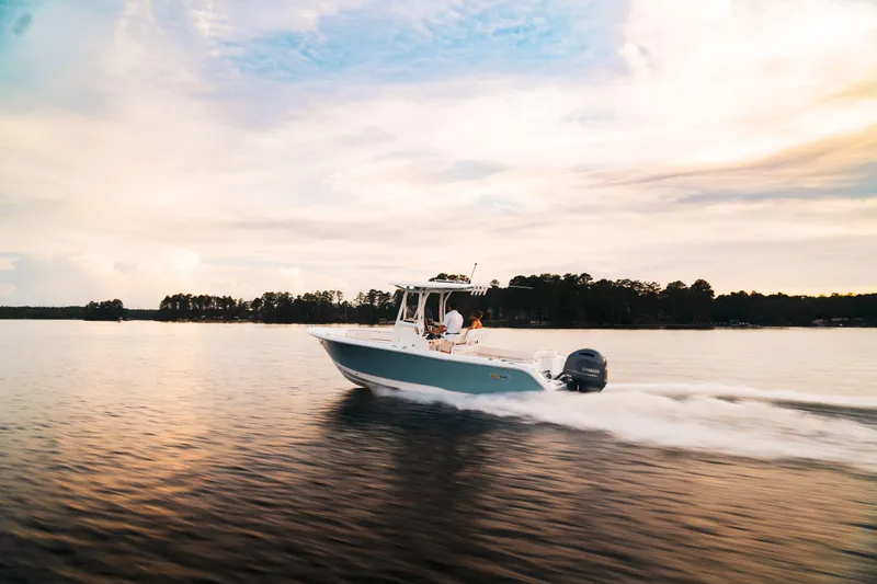 Slide: The Image of 2024 Sea Hunt Ultra 234 boat cruising on a serene lake at sunset. - 2