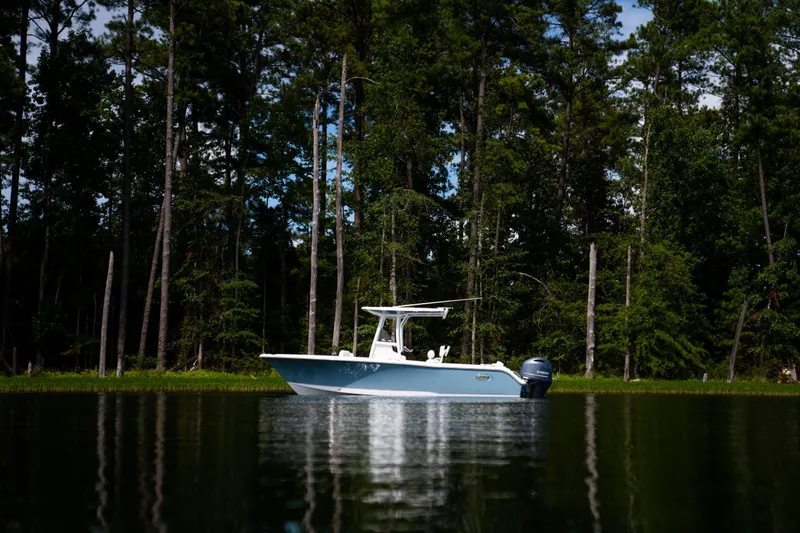 Slide: The Image of 2024 Sea Hunt Ultra 234 boat on a calm lake with forest background. - 8