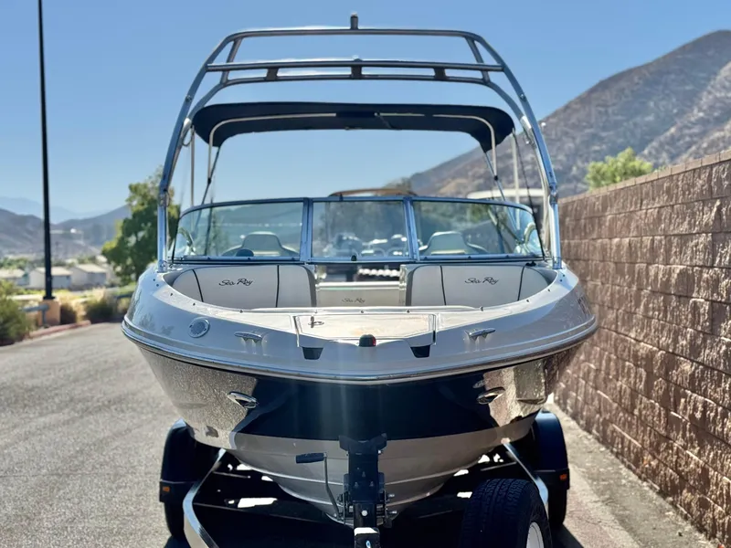 Slide: The Image of 2007 Sea Ray 210 Select boat on trailer, parked near a stone wall, mountainous background. - 2