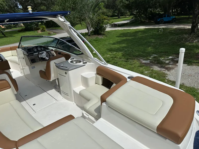 Slide: The Image of 2012 Sea Ray SLX 270 boat interior with tan and white seating, steering console, and lush surroundings. - 15
