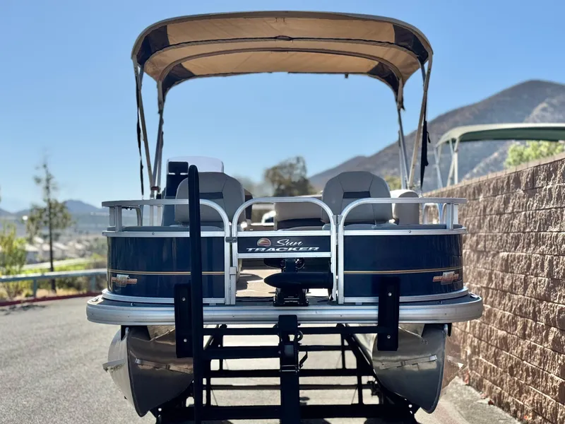 Slide: The Image of 2023 Sun Tracker Bass Buggy 18 DLX pontoon boat with canopy, parked on a sunny day. - 2