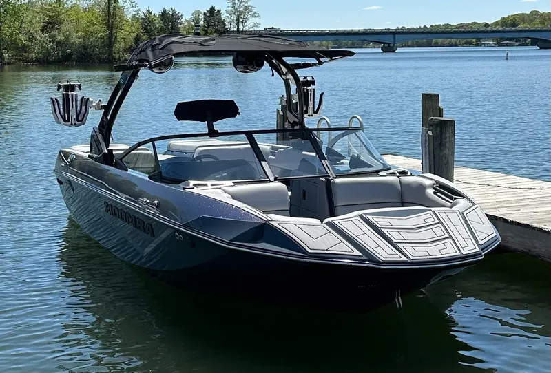 Slide: The Image of 2024 Moomba Kaiyen boat docked on a serene lake with a bridge in the background. - 1