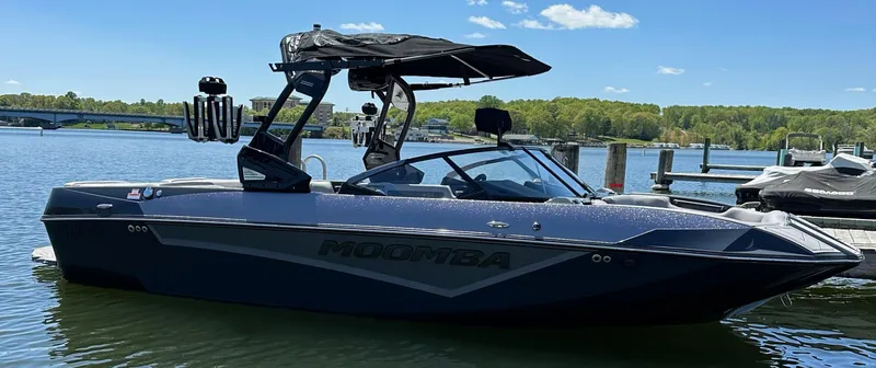 Slide: The Image of 2024 Moomba Kaiyen boat docked on a sunny lake with clear skies. - 2