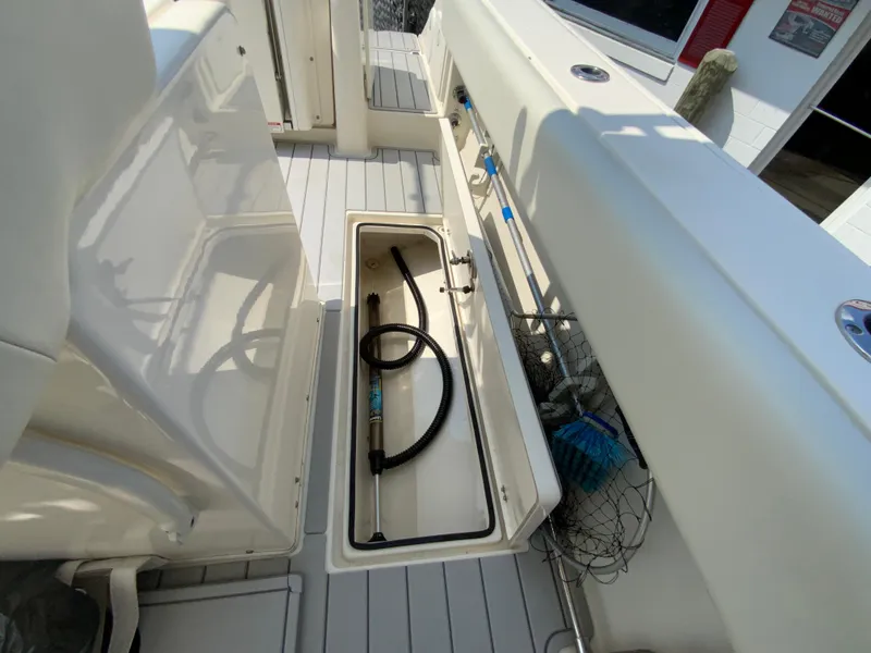 Slide: The Image of 2013 Cobia 296 Center Console boat storage compartment with hose and fishing net. - 34