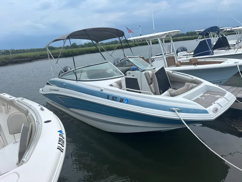 Slide: The Image of 2023 Crownline Eclipse E235 XS boat docked on a calm river under a cloudy sky. - 3