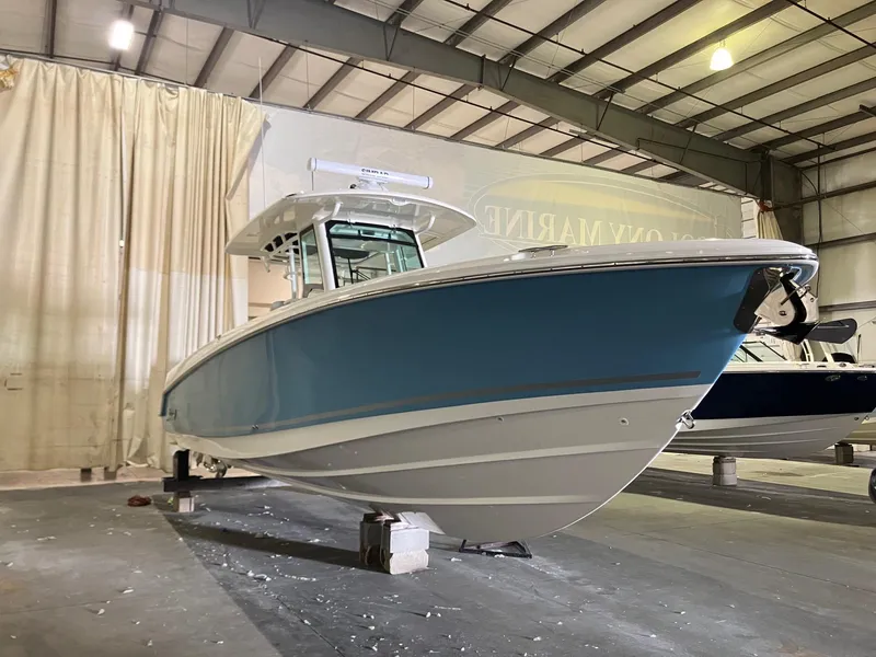 Slide: The Image of 2025 Boston Whaler 330 Outrage boat in a warehouse, showcasing sleek design and blue hull. - 2