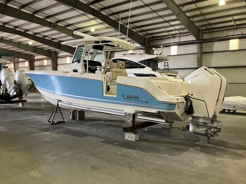 Slide: The Image of 2025 Boston Whaler 330 Outrage boat in a warehouse, featuring dual Mercury engines. - 3