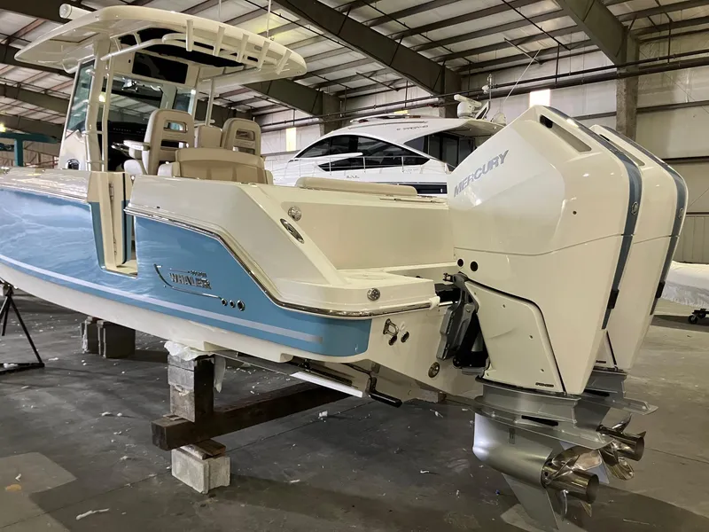 Slide: The Image of 2025 Boston Whaler 330 Outrage boat with dual Mercury engines in a warehouse. - 4