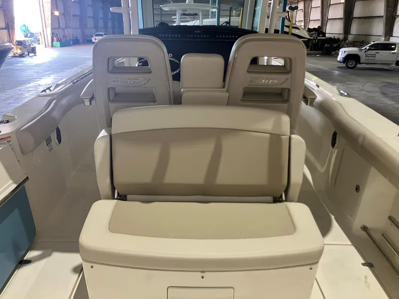 Slide: The Image of 2025 Boston Whaler 330 Outrage boat interior with beige seating in a warehouse setting. - 8