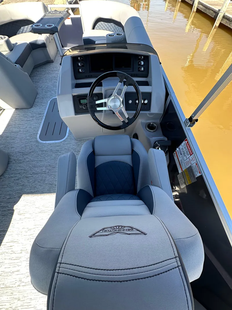 Slide: The Image of 2025 Bennington 23LFB boat interior with steering wheel and seating, docked by the water. - 8