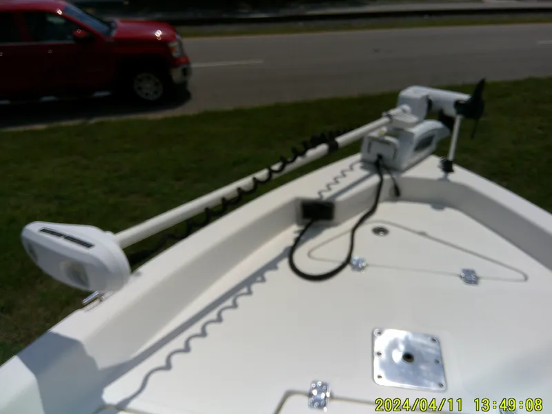Slide: The Image of 2017 NauticStar 2140 Sport boat with trolling motor on deck, parked near a red vehicle. - 13