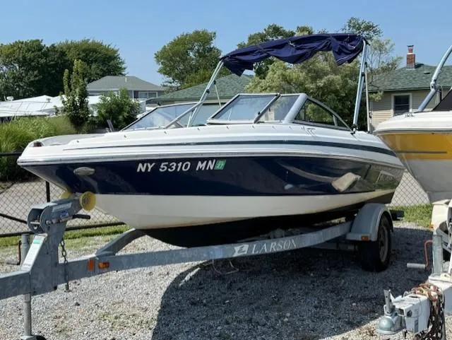 Slide: The Image of 2011 Larson LX 850 boat on trailer, parked outdoors, with blue and white design. - 2