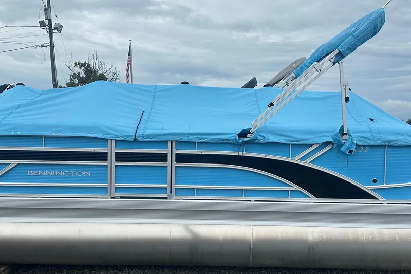 Slide: The Image of 2025 Bennington 22 SSR pontoon boat with blue cover, parked outdoors. - 10