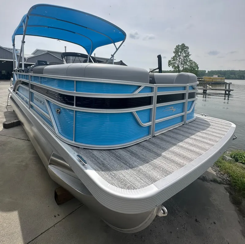Slide: The Image of 2025 Bennington 22 SSR pontoon boat with blue accents docked by a lake. - 3