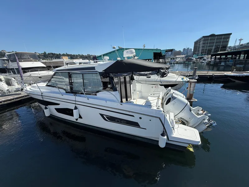 The Image of 2022 Jeanneau NC 1095 Coupe boat docked in a marina under clear blue skies. - 0