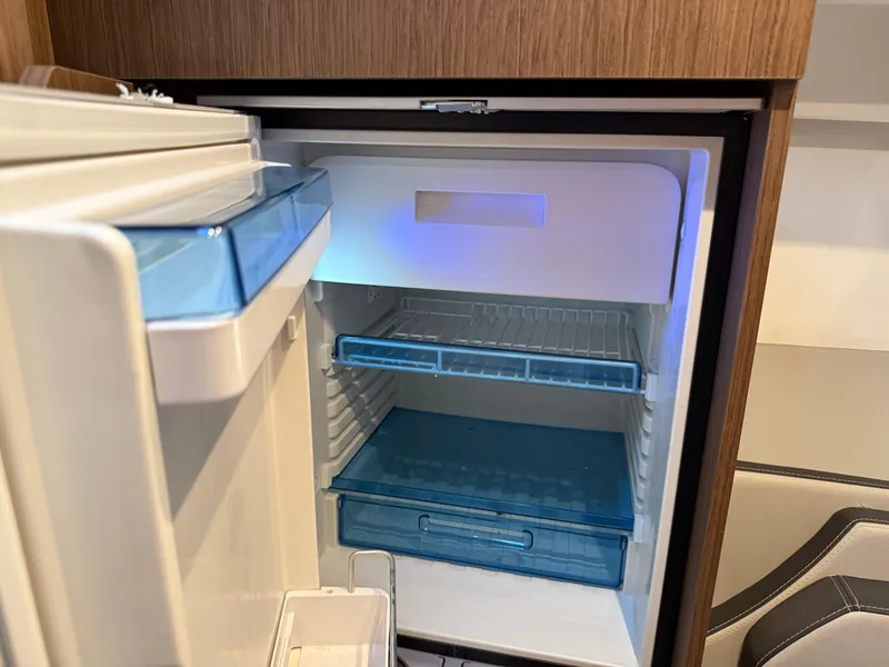 Slide: The Image of Open refrigerator inside 2022 Jeanneau NC 1095 Coupe boat, featuring blue shelves and modern design. - 8