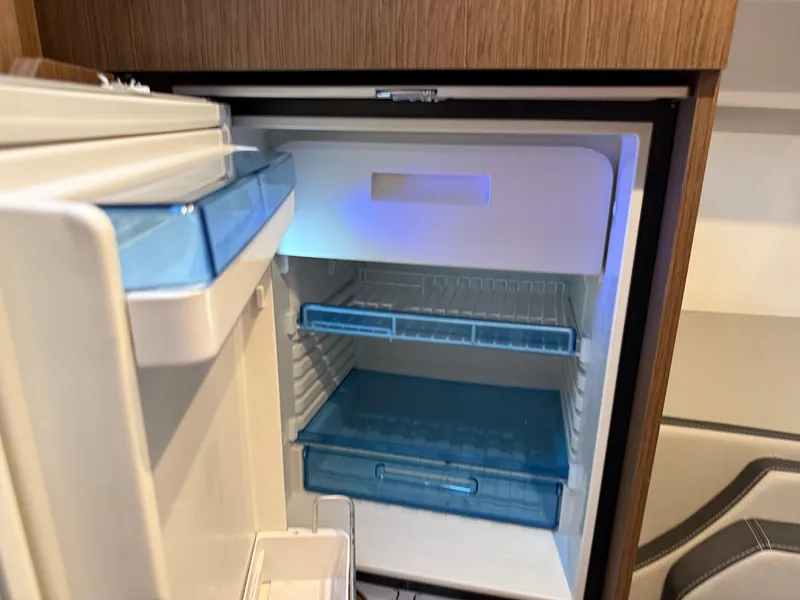 Slide: The Image of Open refrigerator inside 2022 Jeanneau NC 1095 Coupe boat, featuring blue shelves and modern design. - 9