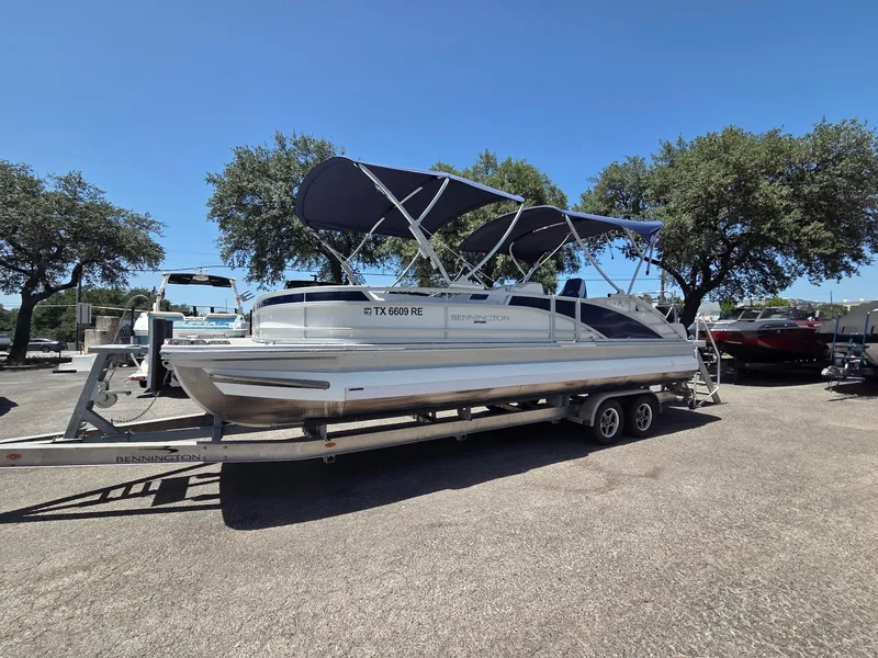 The Image of 2023 Bennington 25RTSB pontoon boat on trailer, parked outdoors under clear blue sky. - 0