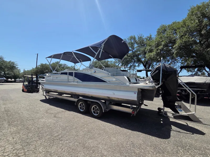 Slide: The Image of 2023 Bennington 25RTSB pontoon boat with canopy on trailer, parked outdoors. - 2
