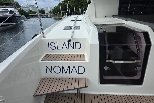 Slide: The Image of 2022 Fountaine Pajot Tanna 47 yacht with "Island Nomad" on steps, docked by water. - 7