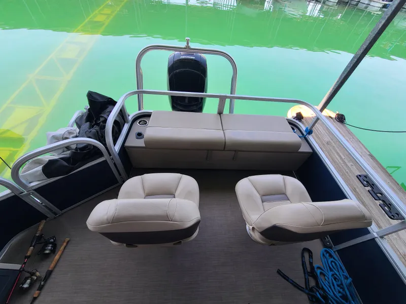 Slide: The Image of 2021 Sun Tracker 22 Fishin Barge interior with seating, fishing rods, and green water backdrop. - 12