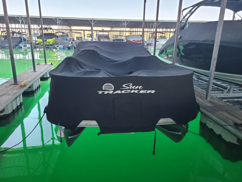 Slide: The Image of 2021 Sun Tracker 22 Fishin Barge covered at marina, docked on vibrant green water. - 5