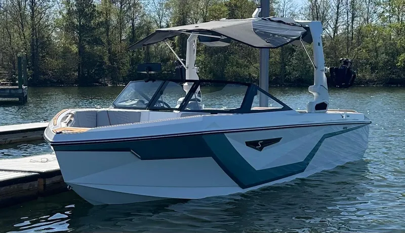 Slide: The Image of 2025 Nautique Super Air Nautique S23 boat docked on a serene lake. - 2