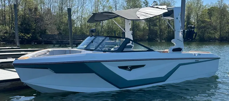 Slide: The Image of 2025 Nautique Super Air Nautique S23 boat docked on a serene lake. - 5