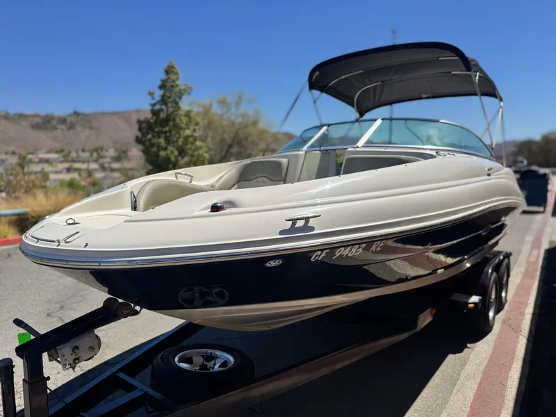 Slide: The Image of 2005 Sea Ray 220 Sundeck boat on trailer, parked on roadside under clear blue sky. - 3