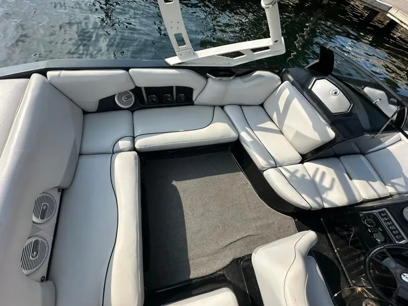 Slide: The Image of 2013 Axis A20 boat interior with white seating and speakers, docked on water. - 16